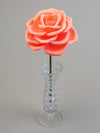 Leafless coral pink crepe paper rose standing in a slender glass vase