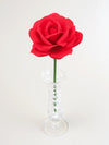 Leafless red cotton paper rose standing in a narrow glass vase against a white backdrop