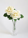 Bouquet of two white cotton paper roses with six green leaves per stem standing in a glass vase against a light grey backdrop
